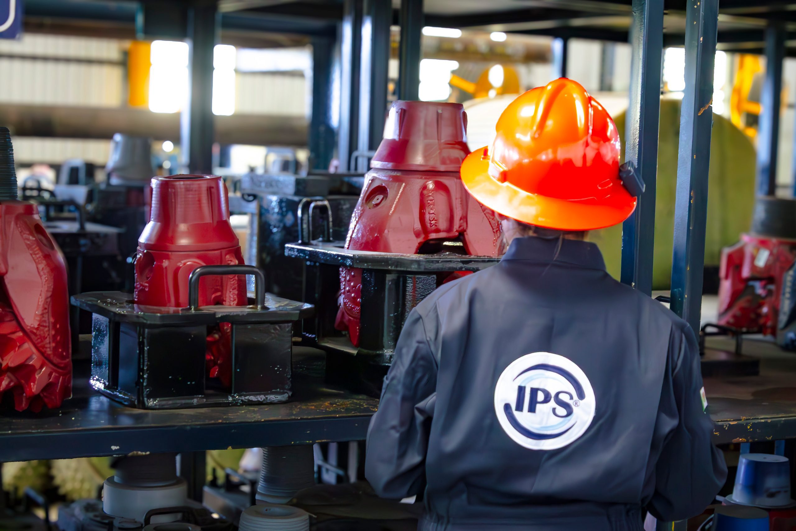Grupo IPS technician in an orange hard hat inspecting drill bits in the workshop