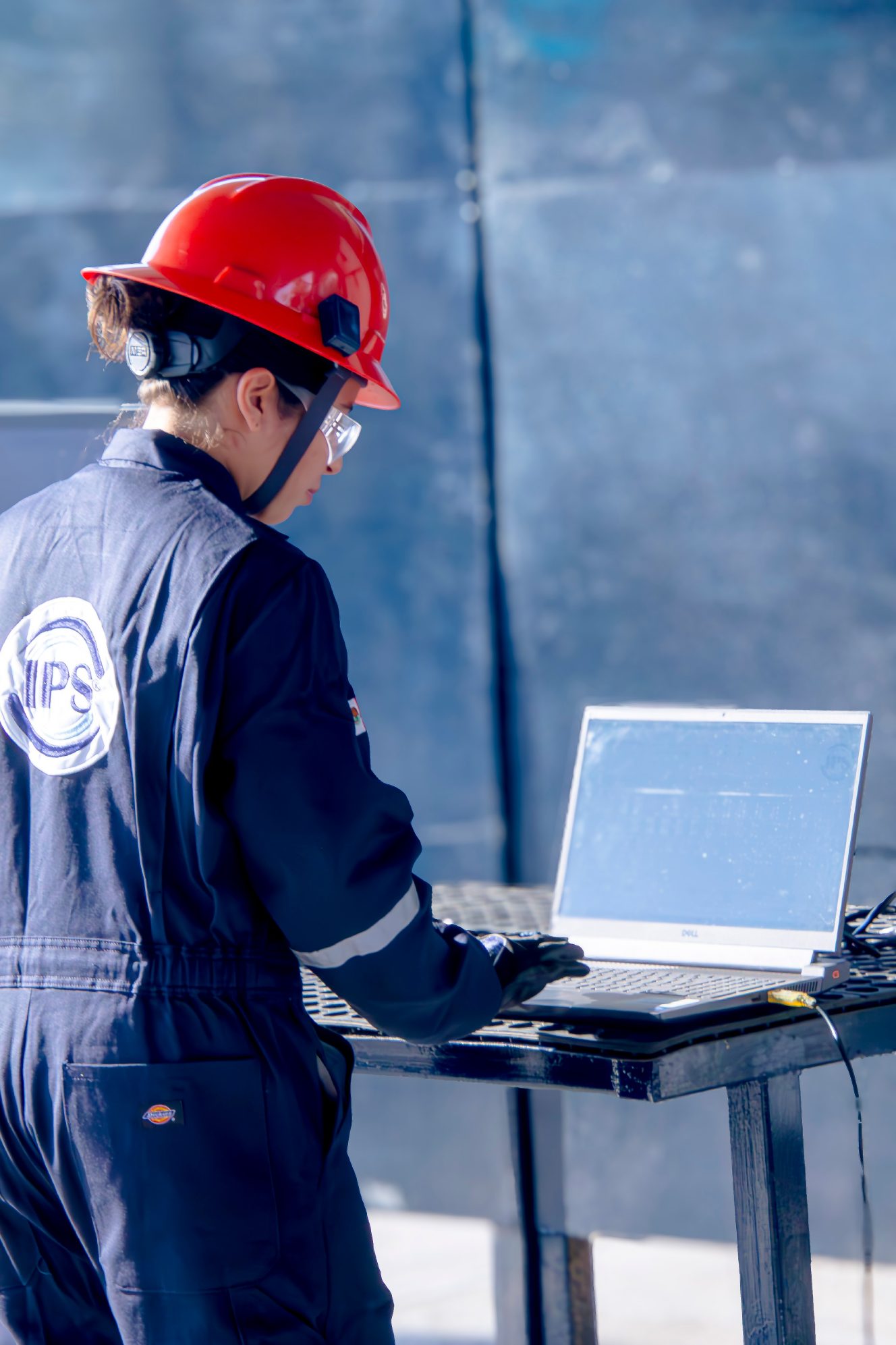 Grupo IPS engineer in a red hard hat working on a laptop in the field
