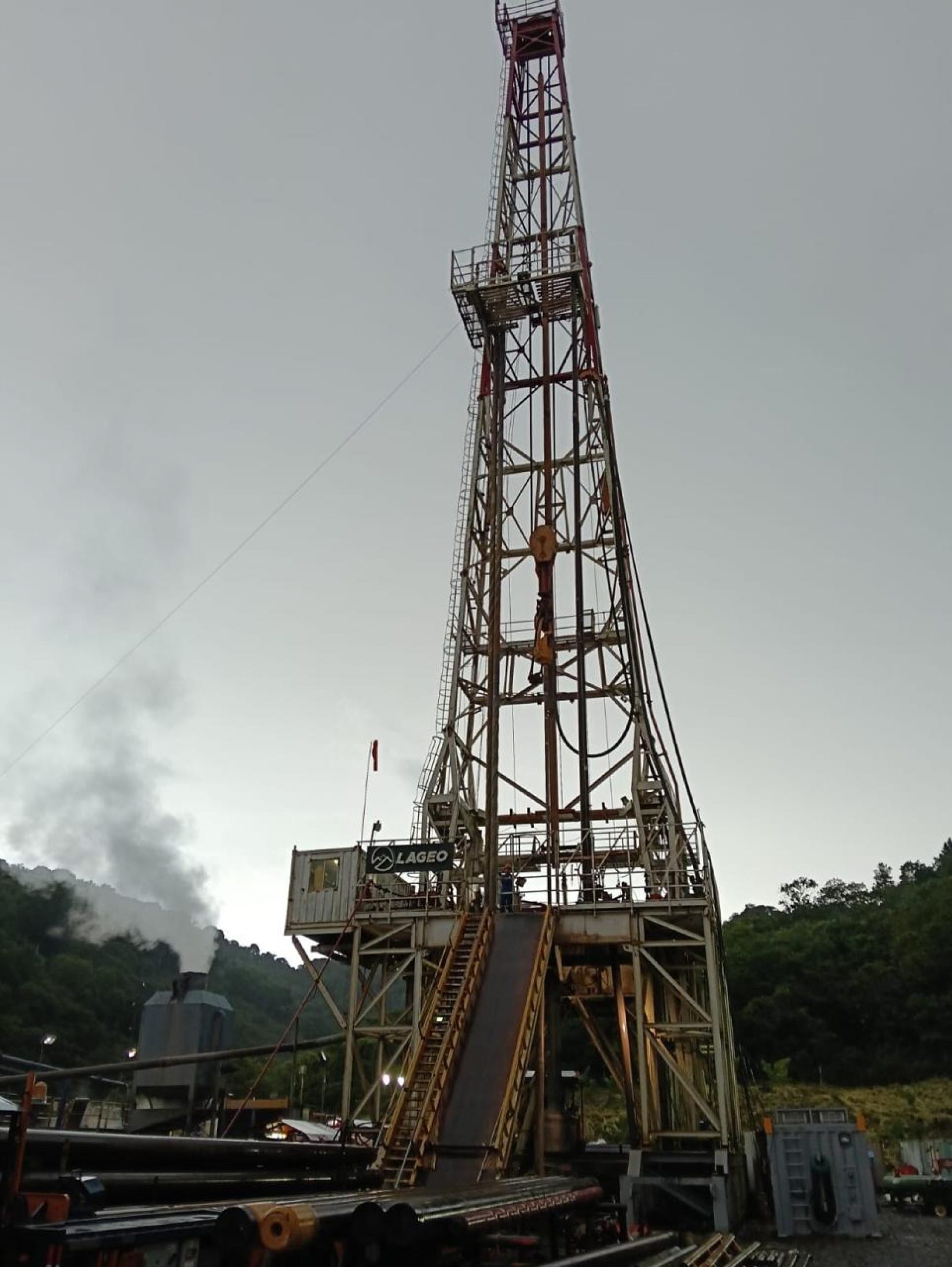 Drilling rig mast with steam rising from a geothermal well